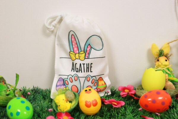 Pochon de Pâques personnalisé pour fille, avec des motifs ludiques d'œufs colorés, de lapins et de poussins, conçu pour cacher des friandises et des petits cadeaux. Personnalisable avec un prénom ou un message
